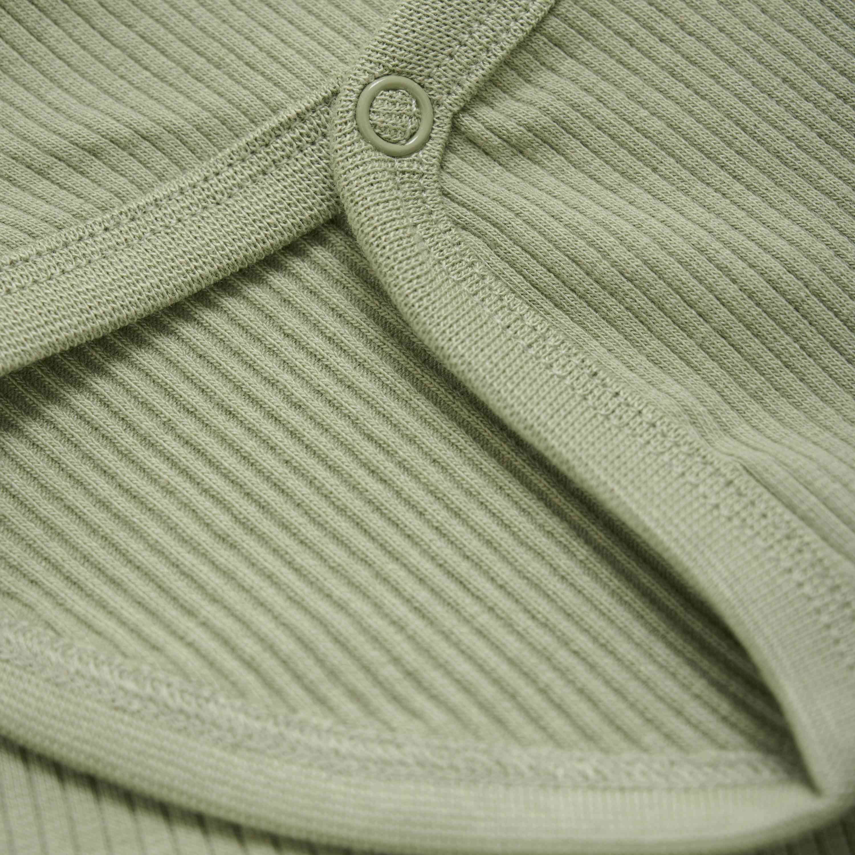 Nahaufnahme eines hellen olivgrünen Rippstoffs mit einem runden, angenähten Knopf. Die Textur des Stoffes ist sichtbar gerippt und der Knopf ist in den GOTS-zertifizierten Bambusstoff eingebettet, was diesem Kleidungsstück Minymo - Body langarm aus Ripp von Minymo ein subtiles Detail verleiht.