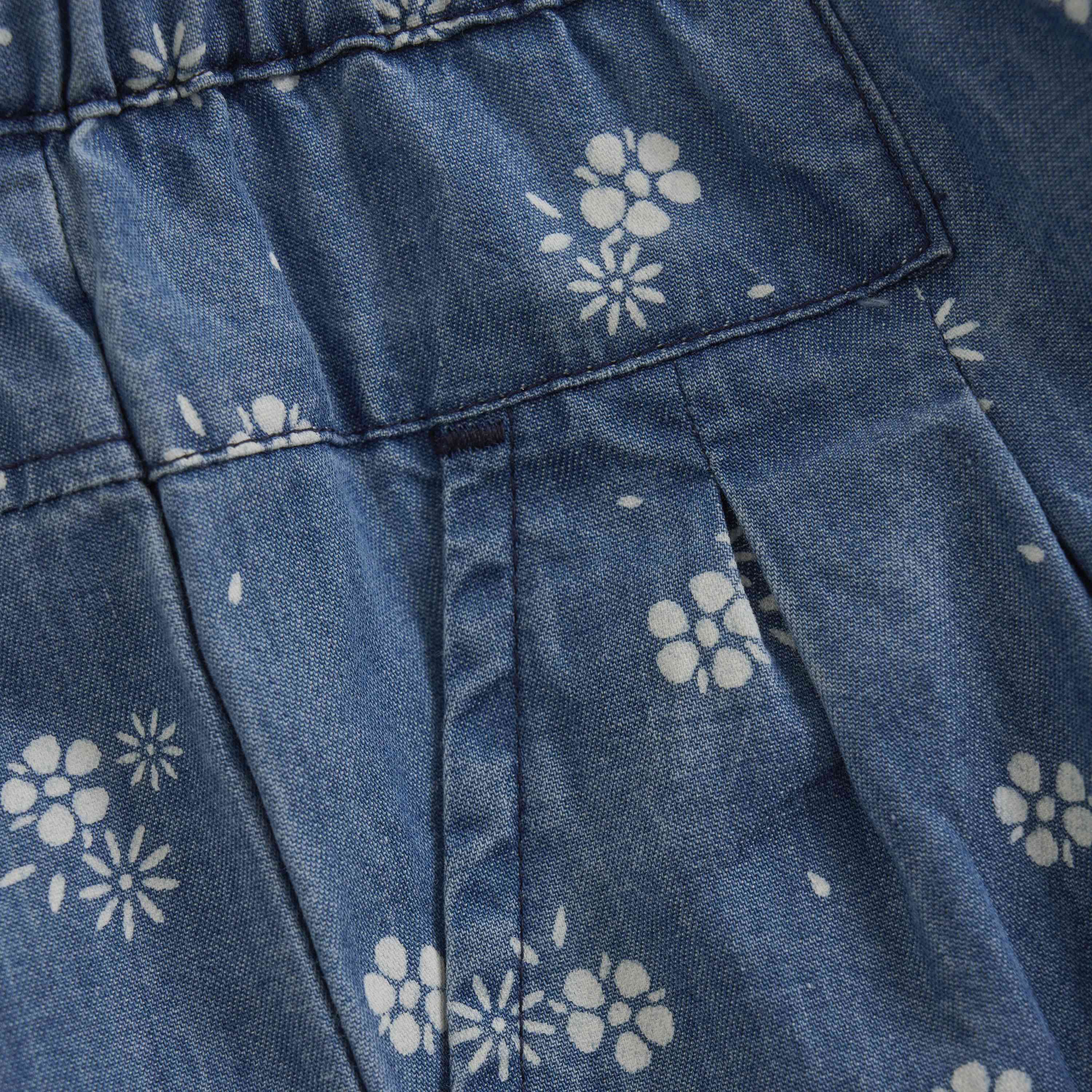 Eine Nahaufnahme eines blauen Stoffes mit weißen Blumenmustern. Der Stoff scheint Falten und Nähte zu haben, möglicherweise von einem Kleidungsstück wie einem Kleid oder Rock. Ideal für die Herstellung hochwertiger Kleidungsstücke wie GOTS-zertifizierter Kleider oder für diejenigen, die Minymo - Chambray-Hosen von Minymo mit einzigartigem Design kaufen möchten.