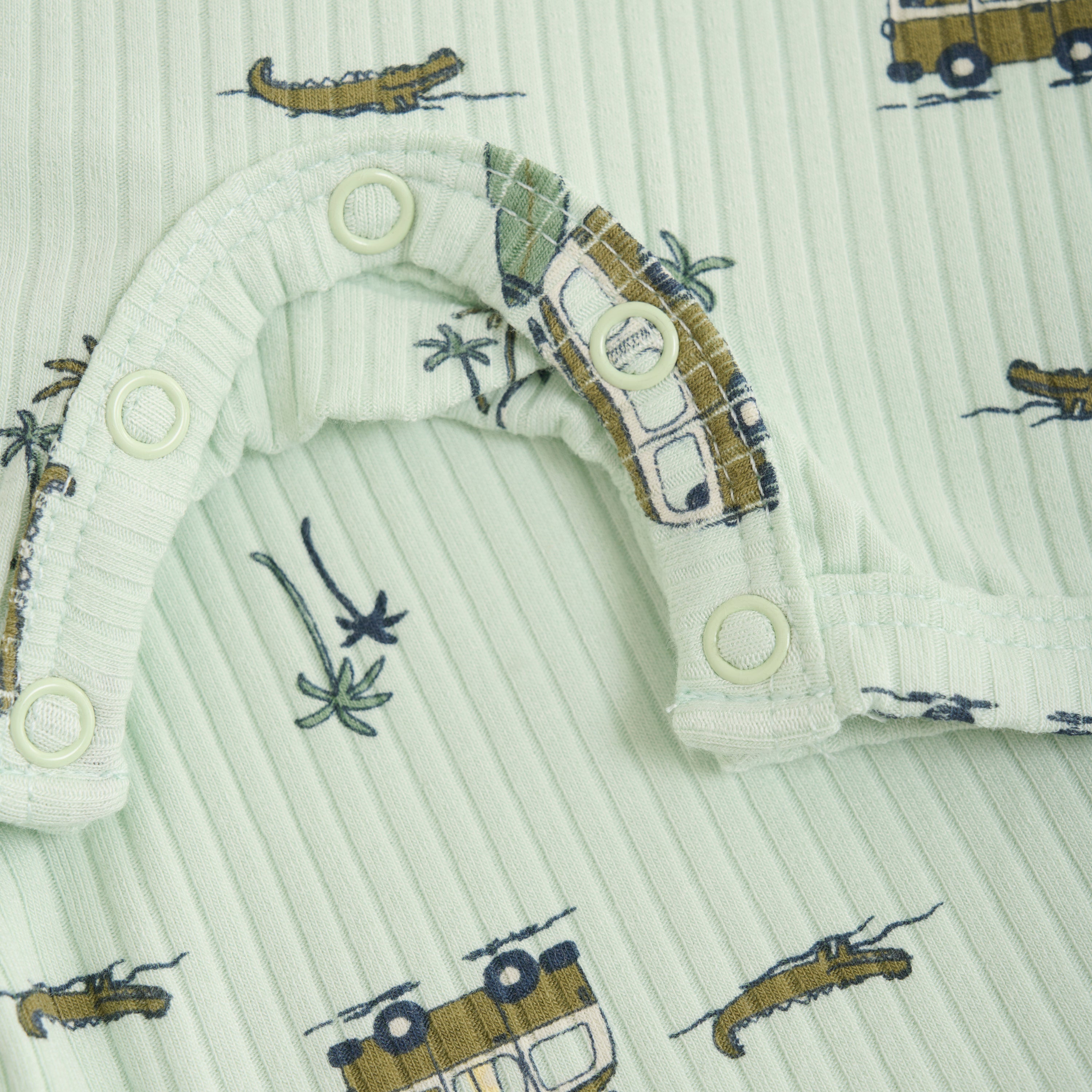 Nahaufnahme eines pastellgrünen, gerippten Minymo - Strampler kurzarm mit Allover-Print mit kleinen Krokodilen-, Baum- und Retro-Vans-Motiven in Braun und Schwarz. Dieses Stoffstück nach Öko-Tex-Standard 100 verfügt über Druckknöpfe an der Schulter und am unteren Saum für einfaches Anziehen.