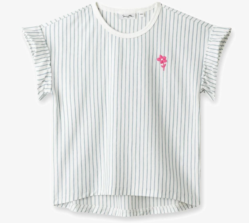 Das Sanetta T-Shirt von Sanetta ist eine kurzärmlige weiße Bluse mit rundem Ausschnitt und dünnen schwarzen Längsstreifen. Es verfügt über gerüschte Ärmeldetails, eine kleine leuchtend rosa gestickte Blume auf der linken Brustpartie und einen stilvollen High-Low-Saum. Hergestellt aus Bio-Baumwolle sorgt es für zusätzlichen Komfort und Nachhaltigkeit.