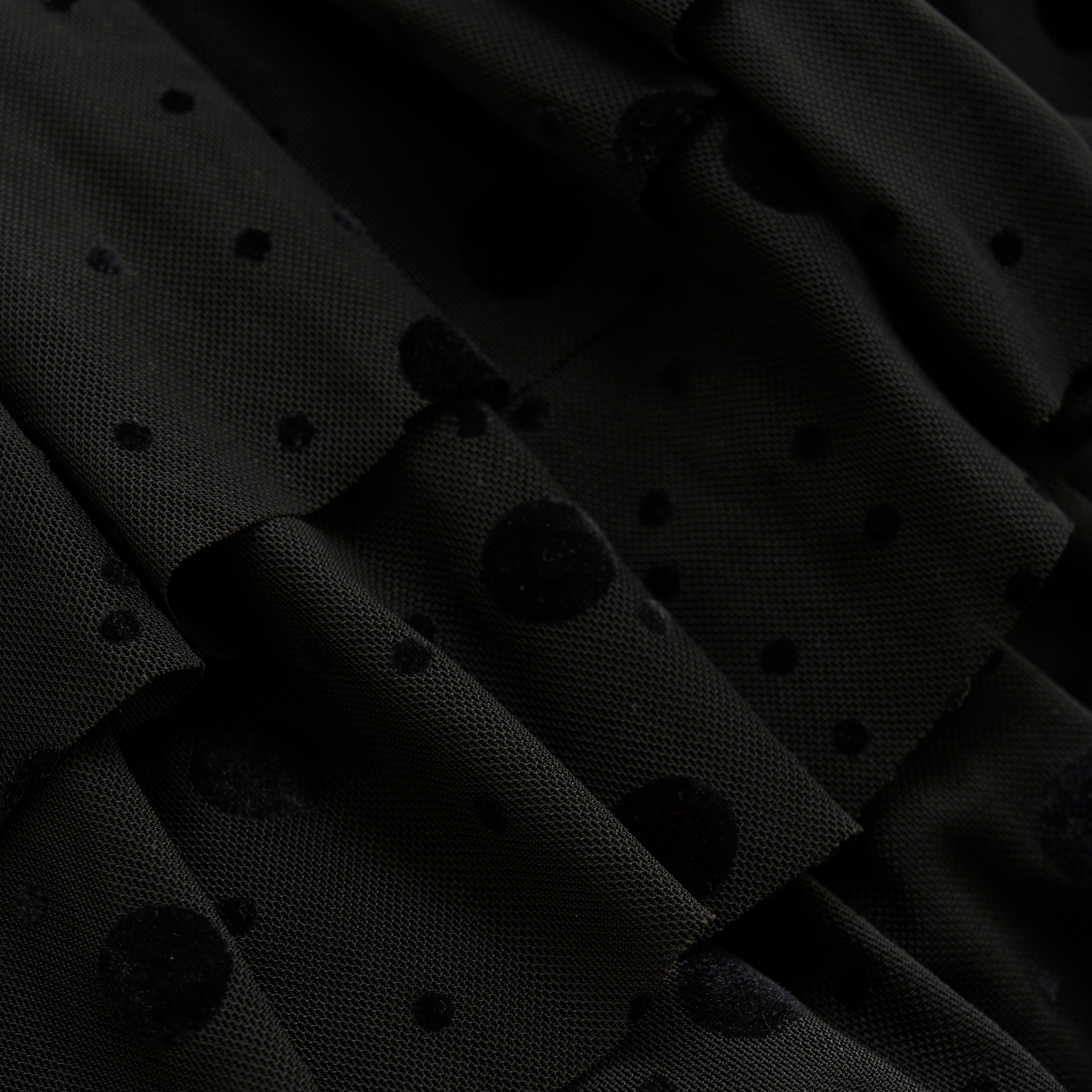 Nahaufnahme von Minymo - Rock, die einen schwarzen Stoff mit einem strukturierten Tupfenmuster zeigt. Das Material scheint geschichtet oder gerafft zu sein, wodurch der Stoffoberfläche ein Gefühl von Tiefe und Dimension verliehen wird, das durch einen subtilen Glitzereffekt noch verstärkt wird.