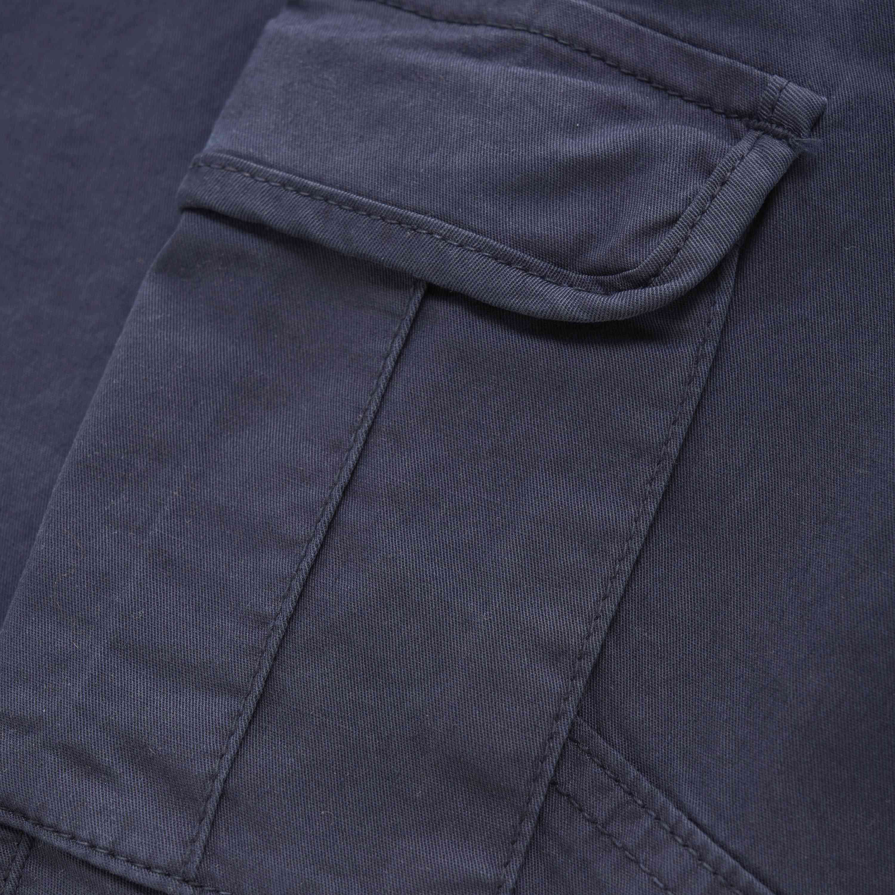 Nahaufnahme eines dunkelmarineblauen Minymo-Twillhosenstoffs mit einer rechteckigen Pattentasche. Die Tasche hat eine einzelne umklappbare Klappe, die mit einer Naht entlang der Kante befestigt ist, und der Stoff scheint leicht strukturiert und robust zu sein, was darauf hindeutet, dass es sich um einen Teil der strapazierfähigen Twillhosen aus einer Baumwollmischung von Minymo handelt.