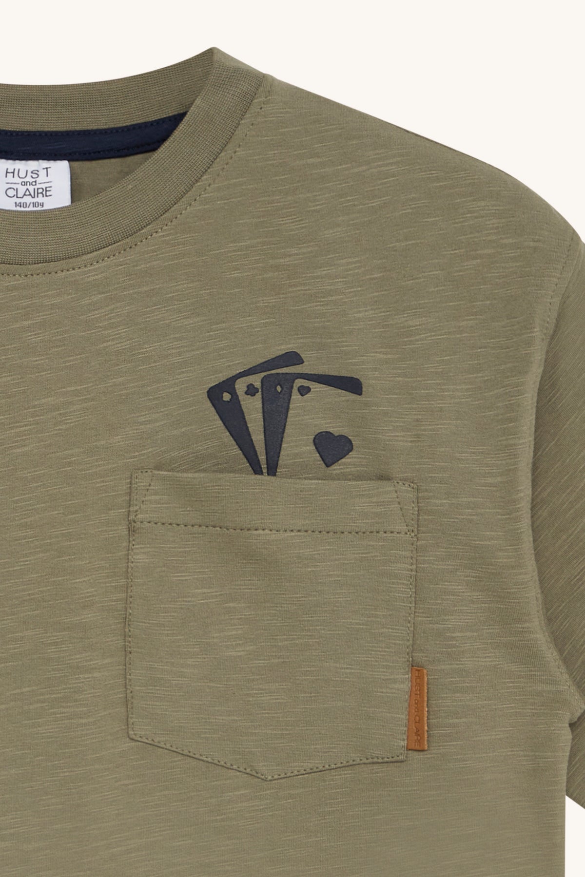 Olivgrünes Hust & Claire - Andi T-Shirt mit kleiner Brusttasche auf der linken Seite. Über der Tasche ist ein Design mit drei Spielkartensymbolen angebracht: zwei Asse und ein Herz. Seitlich an der Tasche ist ein kleines braunes Etikett angebracht. Auf dem Etikett steht „Hust & Claire“, bekannt für ihre mitwachsenden Shirts, erhältlich im kinderartikelgeschäft in Brimensdorf.