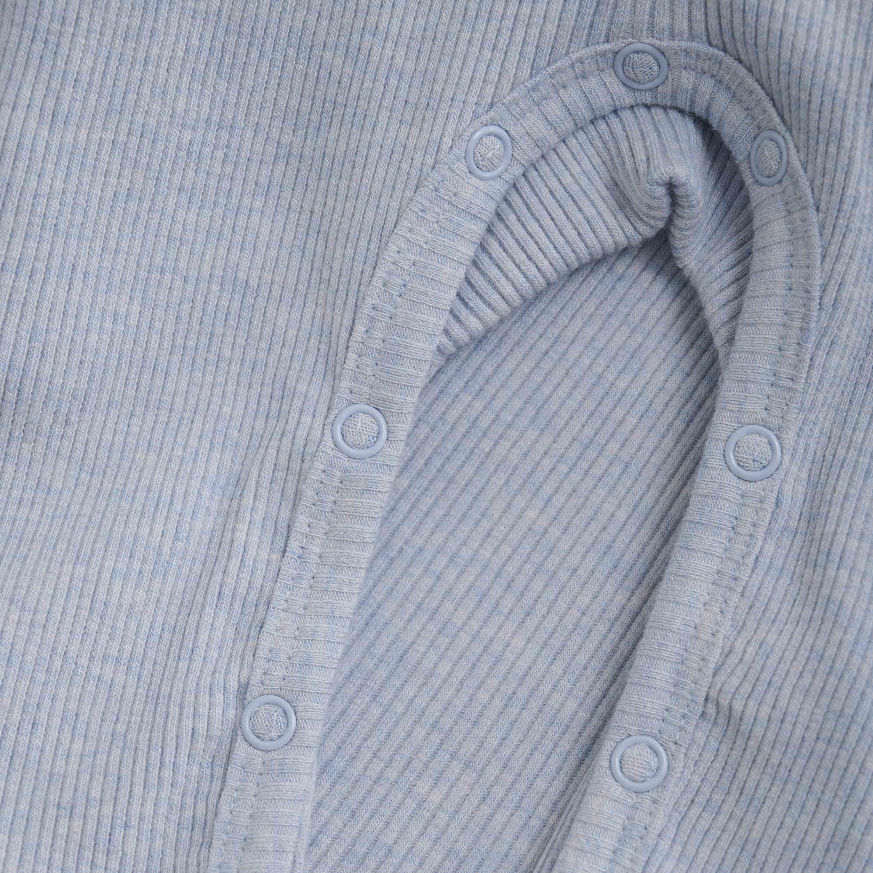 Nahaufnahme eines babyblauen, gerippten Stoffes mit einer Öffnung, die durch Druckknöpfe gesichert ist. Das Material wirkt weich und dehnbar und ist daher perfekt für den Fixoni - Strampler geeignet. Von Fixoni aus TENCEL™ gefertigt, sind die strukturierte Oberfläche und die Knopfdetails deutlich sichtbar.