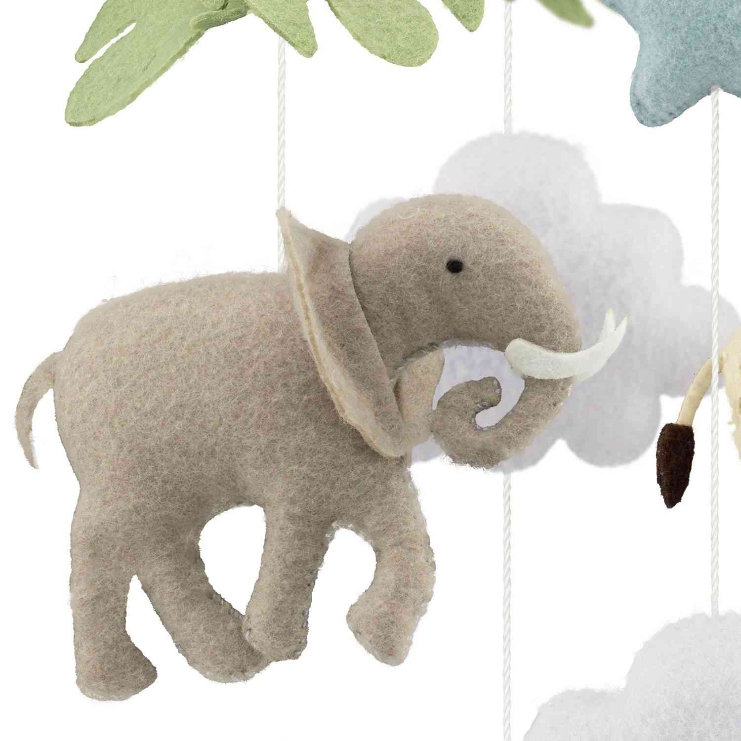 Eine Nahaufnahme eines weichen Elefantenornaments aus Filz, das an einem Mobile hängt. Dieses Ulysse Couleurs d'Enfance - Mobile - Die Savanne von Ulysse Couleurs d'Enfance ist hellgrau mit weißen Stoßzähnen und ist von weiteren Dekorationen umgeben, darunter weiße und blaue Wolkenformen und grüne Blätter, was es zum besten Spielzeug für 4-Jährige macht.