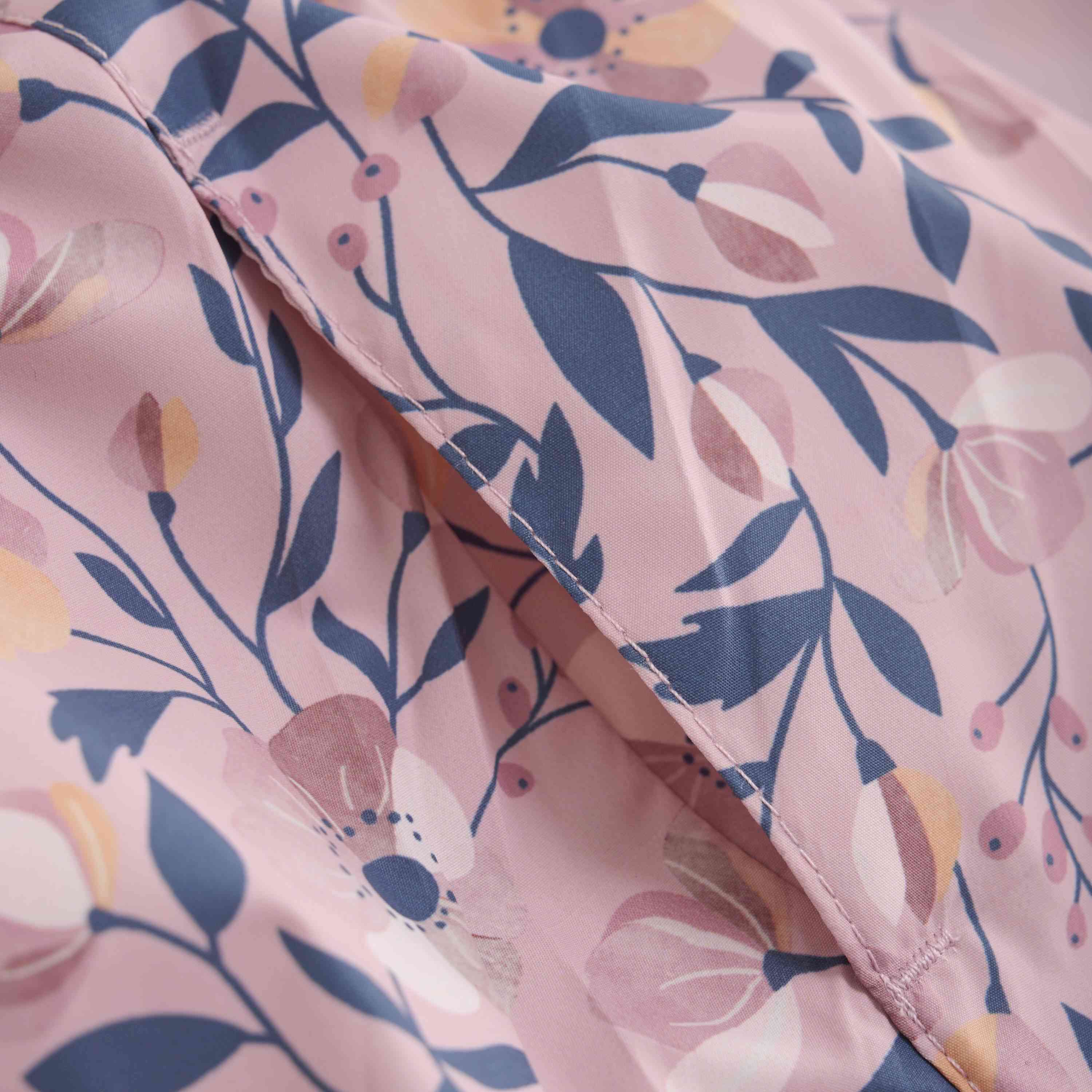 Eine Nahaufnahme eines Stoffes mit rosa Hintergrund und botanischem Muster. Das Design umfasst Blätter, Blumen und Beeren in Blau-, Weiß- und Rosatönen. Die GOTS-zertifizierte *Color Kids - Übergangsjacke* von *Color Kids* scheint leicht gefaltet zu sein, wodurch die Textur und die Details des Drucks zur Geltung kommen.