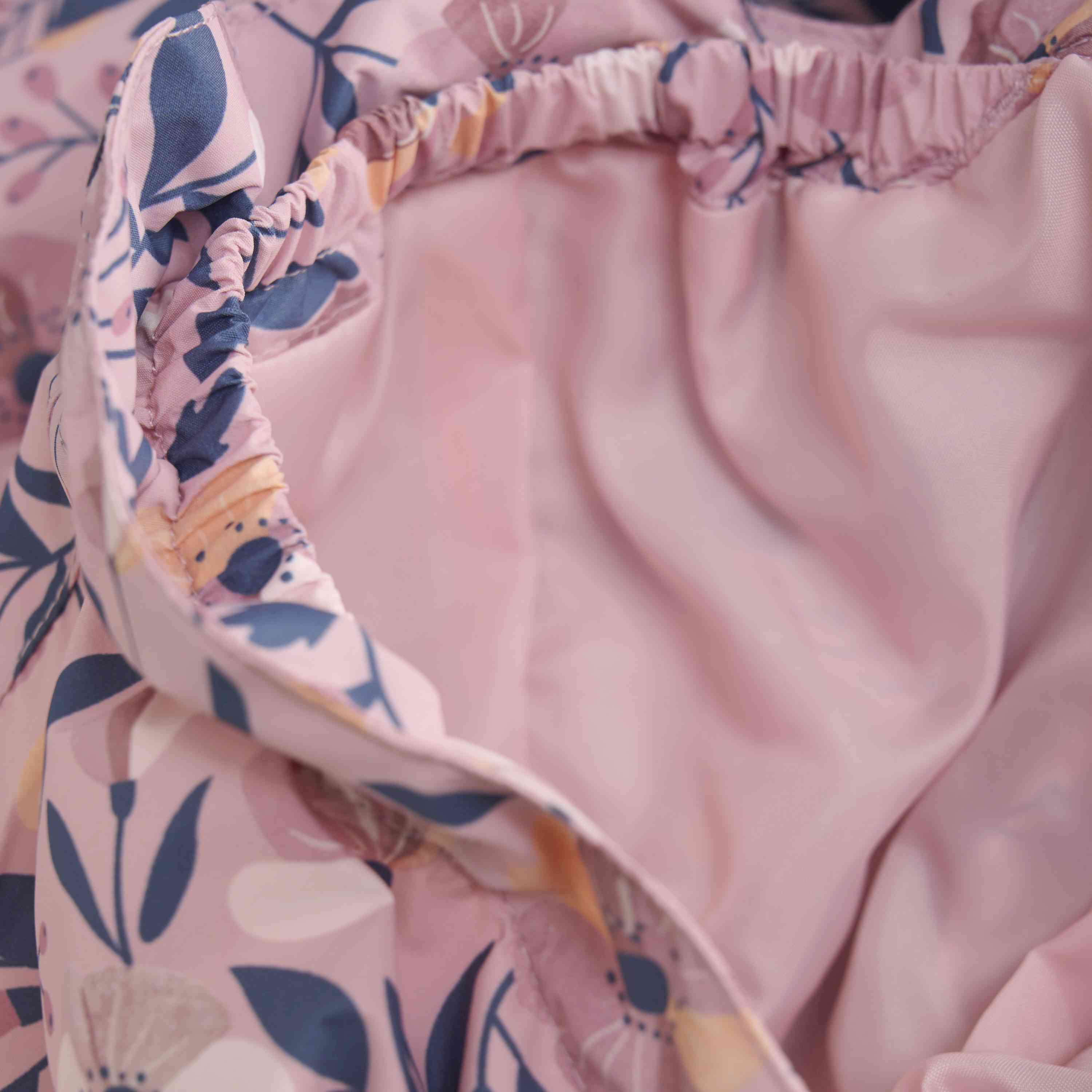 Nahaufnahme eines rosafarbenen Rüschenstoffs mit Blumenmuster und weichen, elastischen Kanten, der einer bezaubernden Color Kids - Übergangsjacke von Color Kids ähnelt. Das leichte Material könnte Teil eines Kleidungsstücks oder Bettzeugs sein. Das Innenfutter ist sichtbar und besteht aus einem einfarbigen hellrosa Material, und das Blumenmuster zeigt verschiedene Blumen in Lila- und Pfirsichtönen.