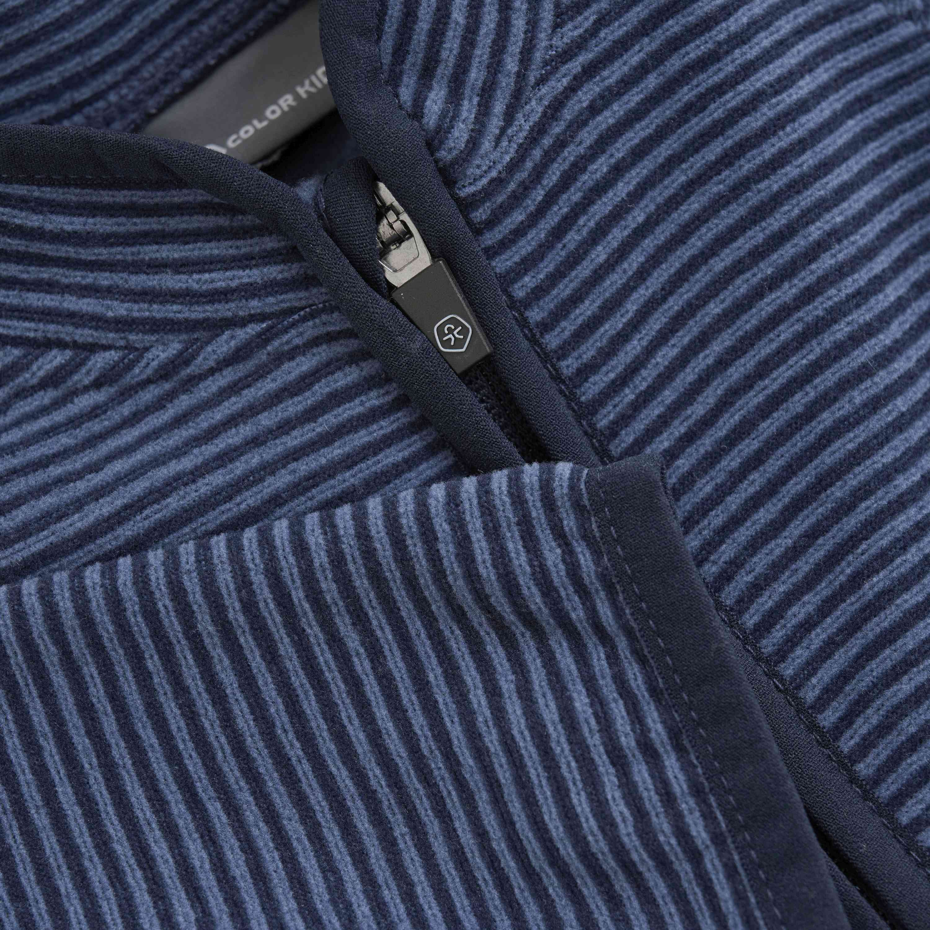 Nahaufnahme eines marineblau-weiß gestreiften Stoffes mit sichtbarem Reißverschluss, der an eine schicke Color Kids - Baby Fleecejacke erinnert. Der Stoff scheint weich zu sein, möglicherweise aus GOTS-zertifizierter Baumwolle oder einem ähnlichen Material. Das Bild konzentriert sich auf die Details der Stoffstruktur und des Reißverschlussmechanismus.