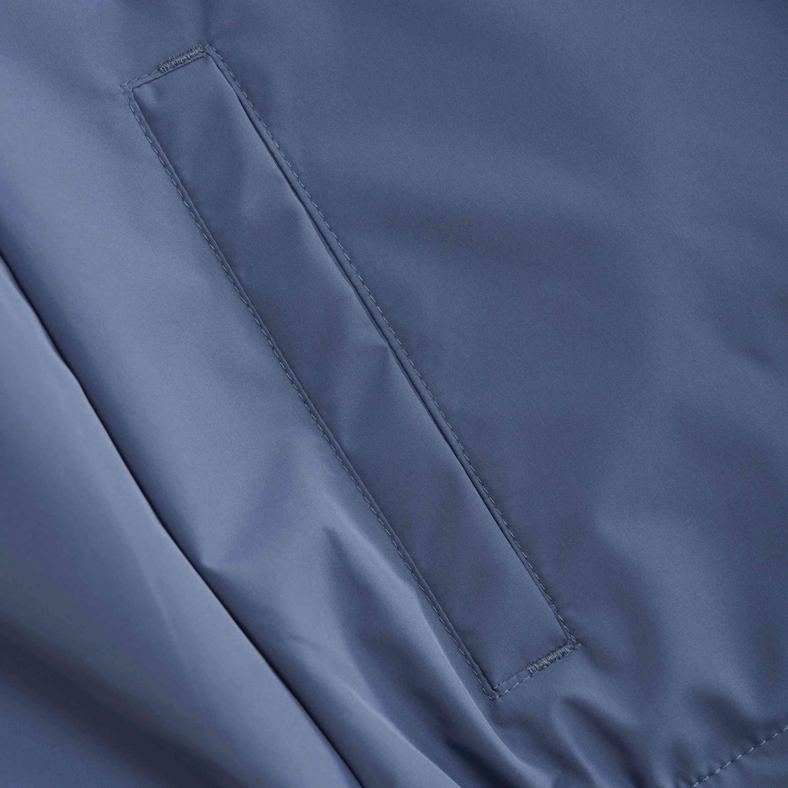 Nahaufnahme einer blauen Stoffoberfläche mit einer rechteckigen, vertikal ausgerichteten Tasche. Die Naht und die saubere Naht um die Tasche herum sind sichtbar und zeigen die Handwerkskunst des GOTS-zertifizierten Kleidungsstücks. Der Stoff wirkt glatt und leicht glänzend. Dies ist die Color Kids - Jacke von Color Kids.