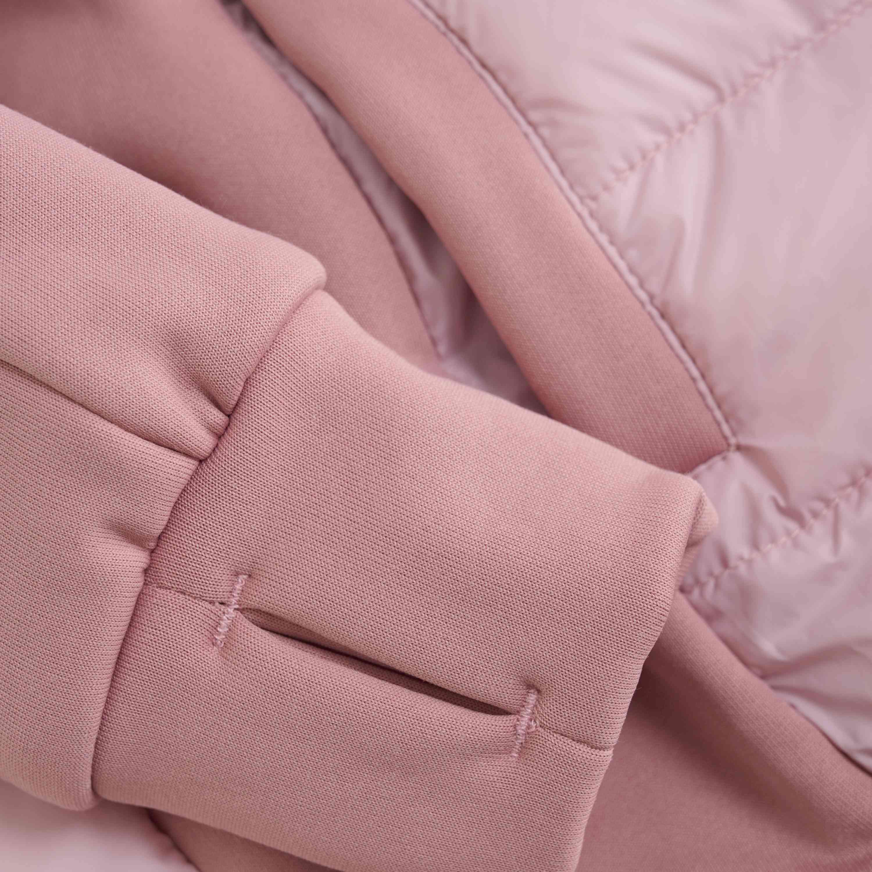 Nahaufnahme einer hellrosa Color Kids - Hybrid-Fleecejacke, die die Ärmel und einen Teil des Körpers zeigt. Der Stoff scheint eine Mischung aus weichem, gestepptem Material und einem glatten, sweatshirtähnlichen Material zu sein, mit sichtbaren Nähten und Nahtdetails, die den GOTS-Standards entsprechen.