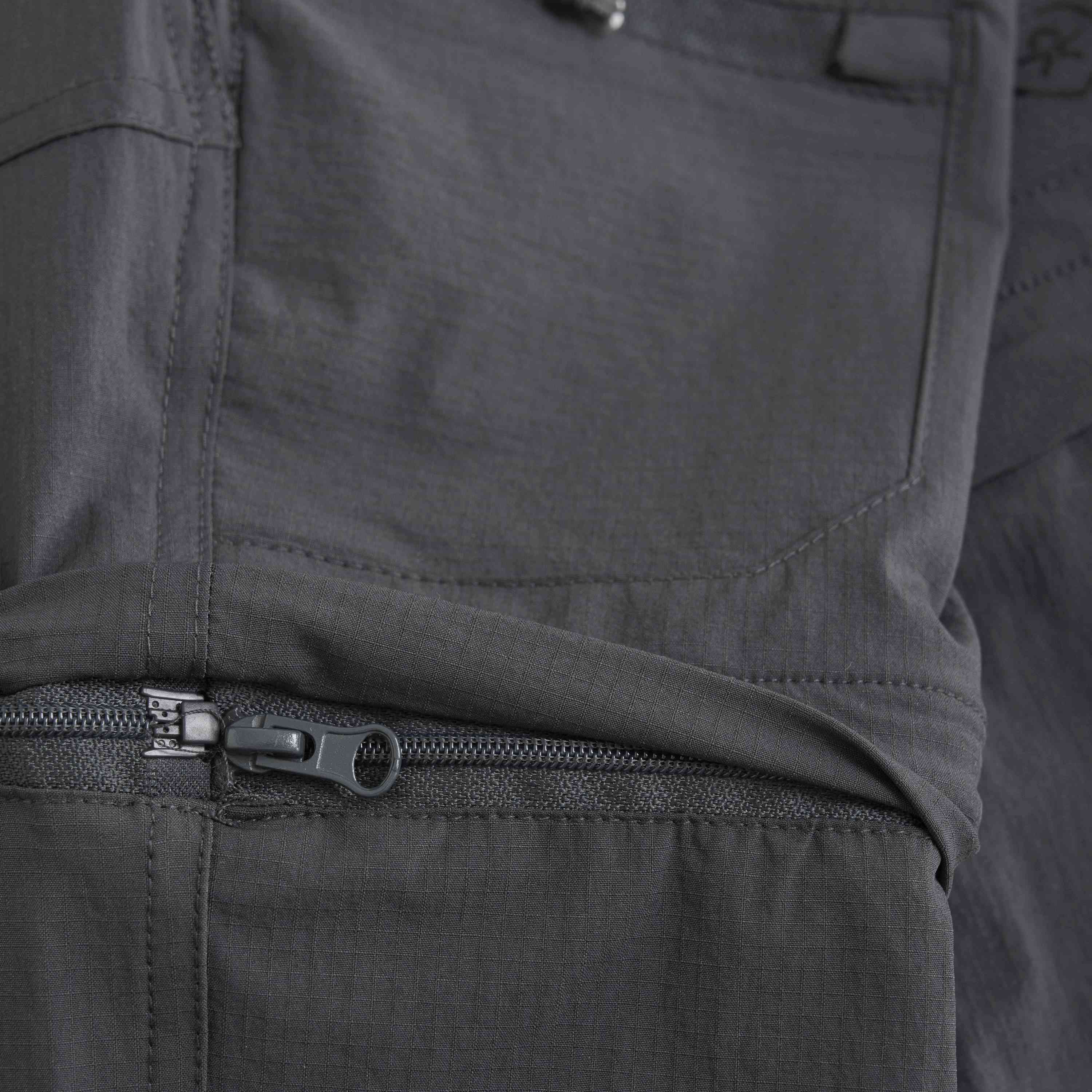 Nahaufnahme einer dunkelgrauen Hose mit Fokus auf einer Reißverschlusstasche. Der Stoff scheint leicht und leicht strukturiert zu sein, mit sichtbaren Nähten und Nähten. Der Reißverschluss ist teilweise geöffnet und gibt den Blick auf das Innere der Tasche frei. Perfekt für jedes Outfit, von Color Kids - Pants Stretch W. Zip Off von Color Kids bis hin zu Abendgarderobe.