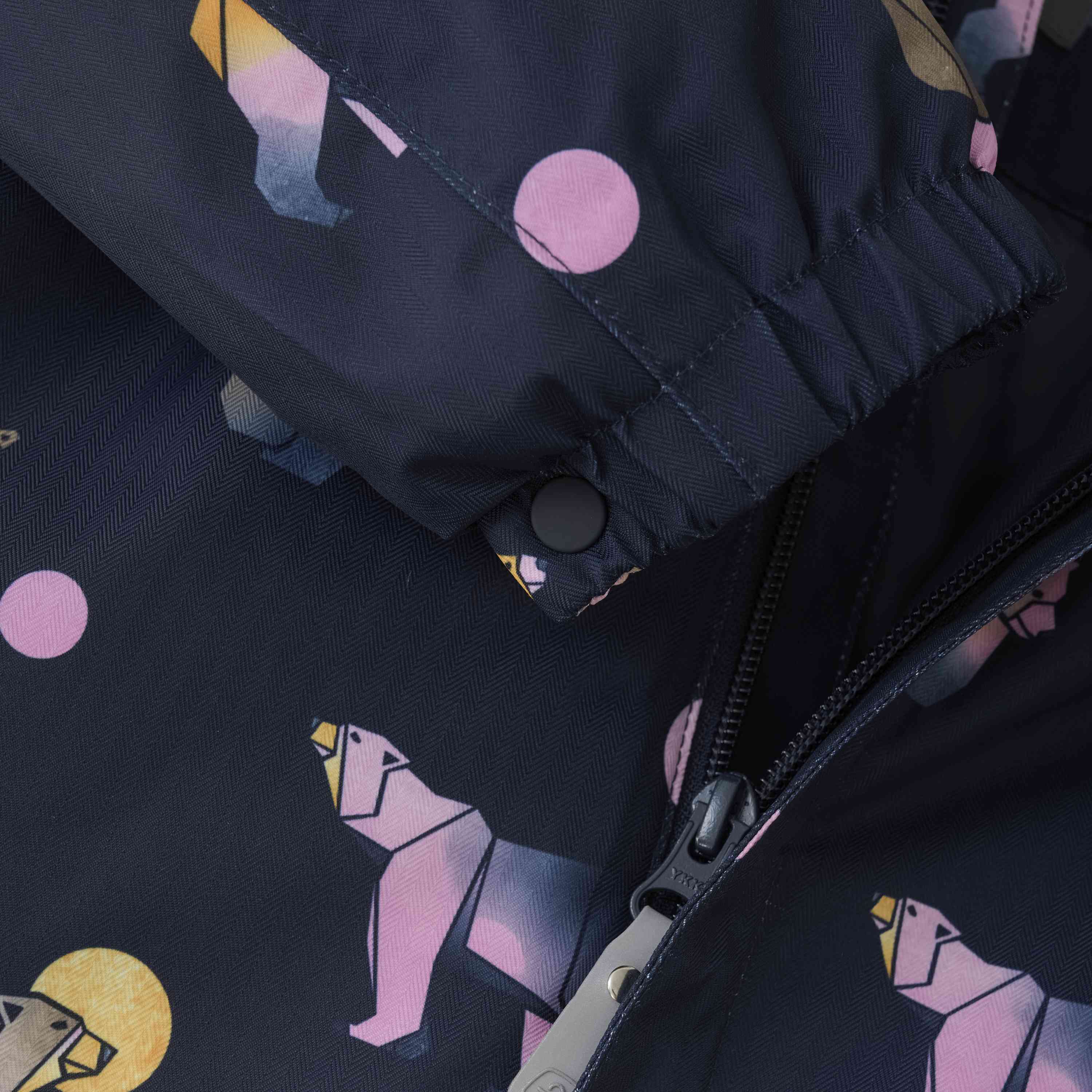 Nahaufnahme des Color Kids – Overalls – AOP von Color Kids. Zu sehen ist eine schwarze Jacke mit einem lebhaften Muster aus geometrischen Bärenmotiven und verstreuten rosa Punkten. Das Bild konzentriert sich auf die Ärmel und die teilweise mit Reissverschluss versehene Vorderseite, wodurch das komplizierte Muster und die Textur des Stoffes hervorgehoben werden. Beschreibung für weitere Einzelheiten folgt.