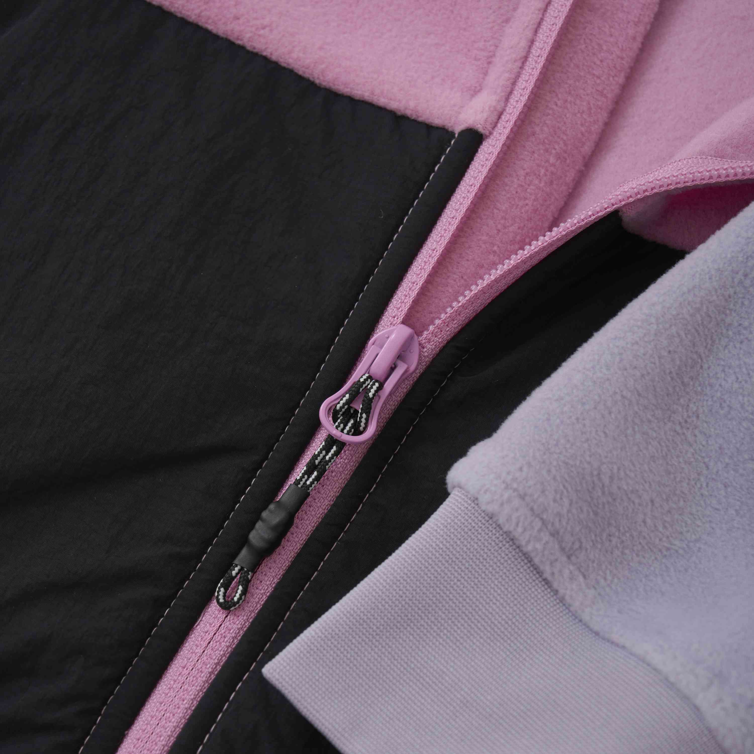 Nahaufnahme eines Reissverschlusses an der Color Kids Fleecejacke – Colorblock mit rosa Reissverschlussschieber. Das Jackenmaterial besteht aus rosa Fleece, schwarzem Stoff und hellblauem Fleece. Die Nähte und die Textur der Stoffe sind deutlich erkennbar.
