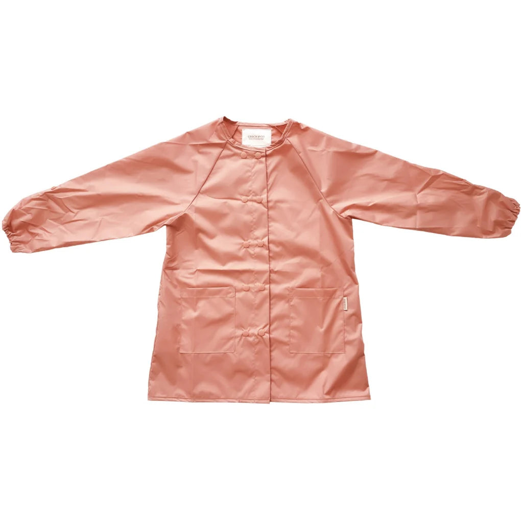 Ein langärmliger rosa Kittel oder eine Jacke mit elastischen Bündchen und offenem Schnitt vorne. Der Grech & Co. - Malkittel für Kinder scheint aus einem glänzenden, wasserabweisenden Material gefertigt zu sein und hat ein schlichtes, funktionales Design.