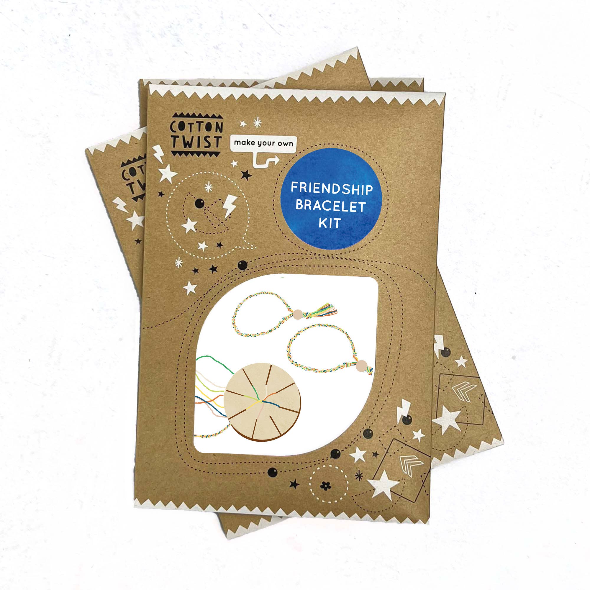 In zwei braunen Kartonverpackungen befindet sich das DIY Freundschaftsarmband-Set von Cotton Twist. Die Verpackung zeigt einen blauen Kreis mit dem Text „Friendship Bracelet Kit“, Abbildungen von Sternen, Kreisen und einer Übersicht mit Materialien zum Basteln des Armbands, darunter Fäden und ein Scheibenwerkzeug. Das Kinder Bastelset ist plastikfrei.