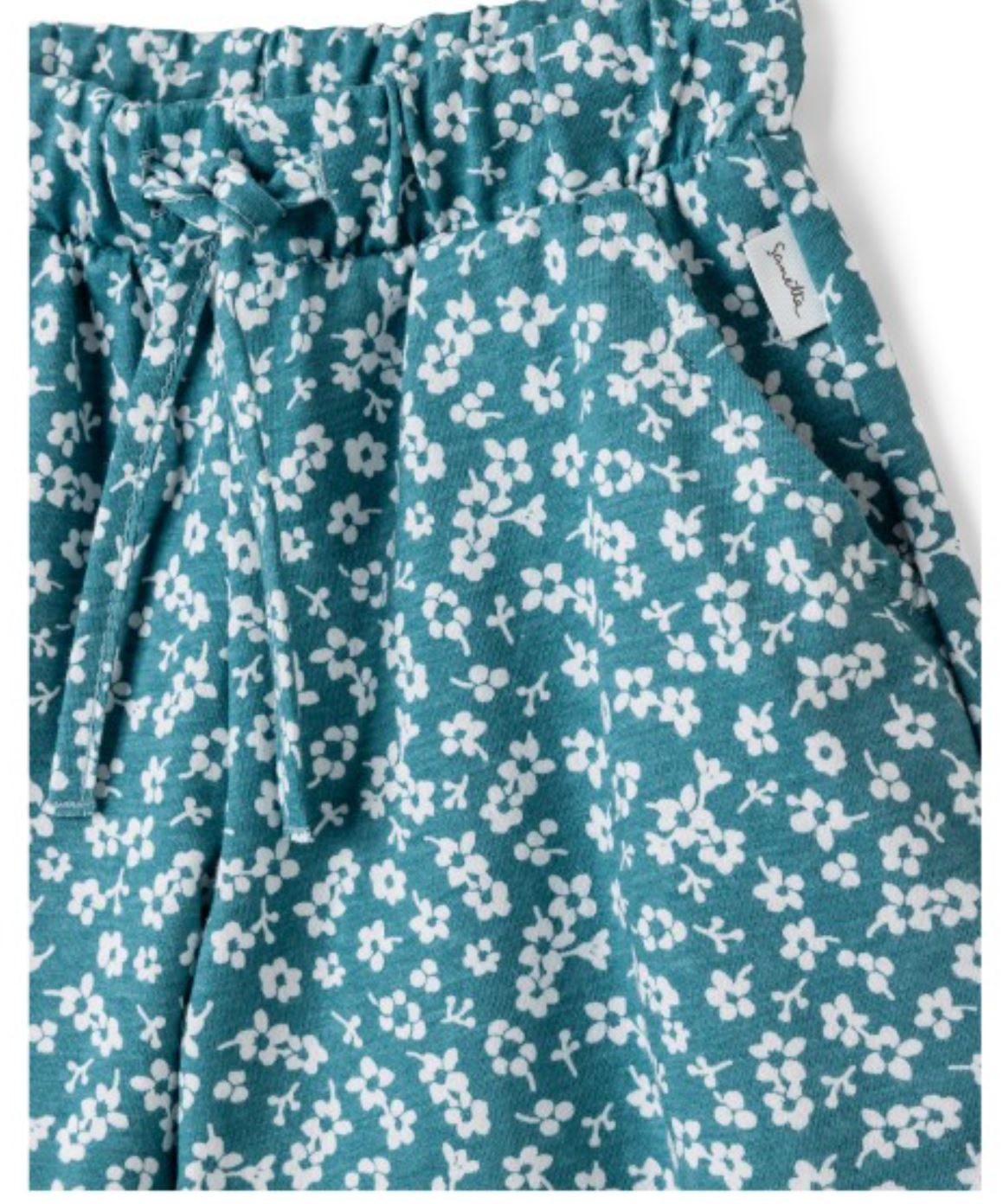 Nahaufnahme der Sanetta-Hose, ein Paar blaugrüne Shorts mit einem weißen Blumenmuster auf der gesamten Oberfläche. Die Sanetta-Shorts haben einen elastischen Bund mit Kordelzug, Vordertaschen und ein kleines Markenetikett an der Seite. Hergestellt aus weichem und bequemem Bio-Baumwolle-Stoff.