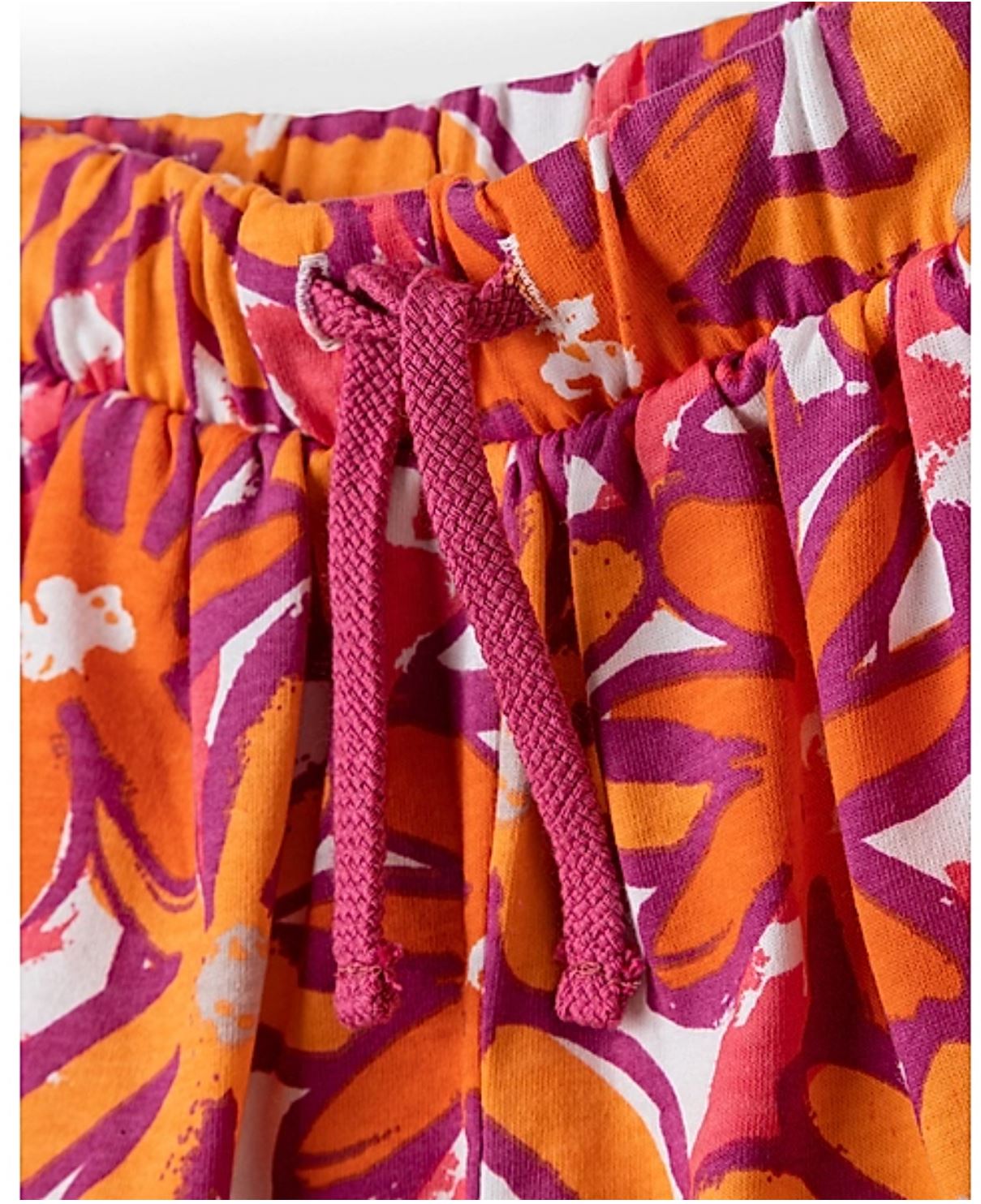 Nahaufnahme eines Paars lebhafter Sanetta-Hosenshorts von Sanetta mit einem Allover-Blumenmuster in Orange-, Lila-, Rosa- und Weißtönen. Die Shorts haben einen elastischen Bund mit einem kastanienbraunen Kordelzug in der Mitte, der für eine verstellbare Passform sorgt.