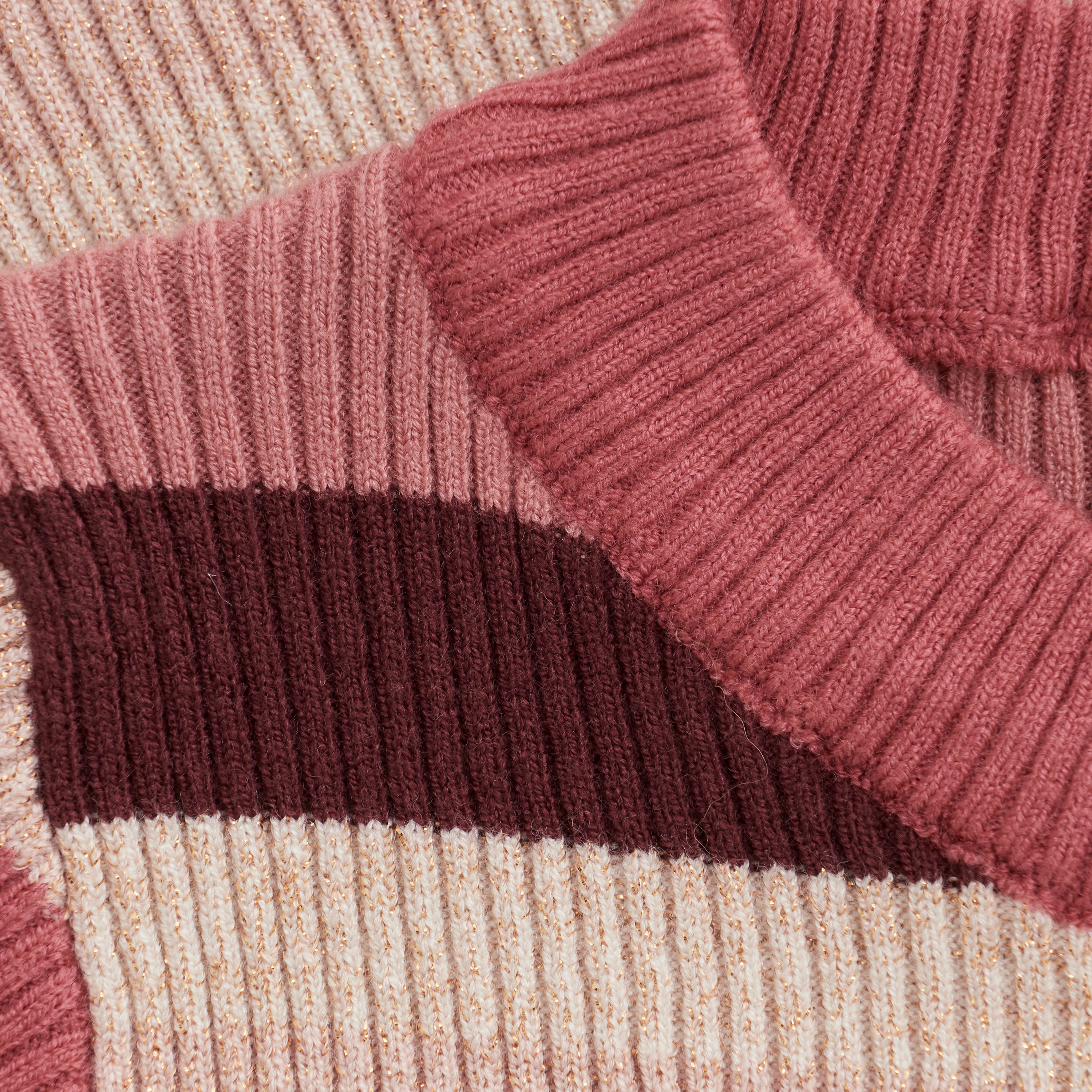 Nahaufnahme eines gestrickten Minymo-Kleides mit gerippter Struktur. Der Pullover hat einen rosa Kragen und horizontale Streifen in Rosatönen, darunter ein dunklerer kastanienbrauner Streifen. Das Strickmaterial ist sichtbar dick und gemütlich mit einem subtilen Glitzereffekt.