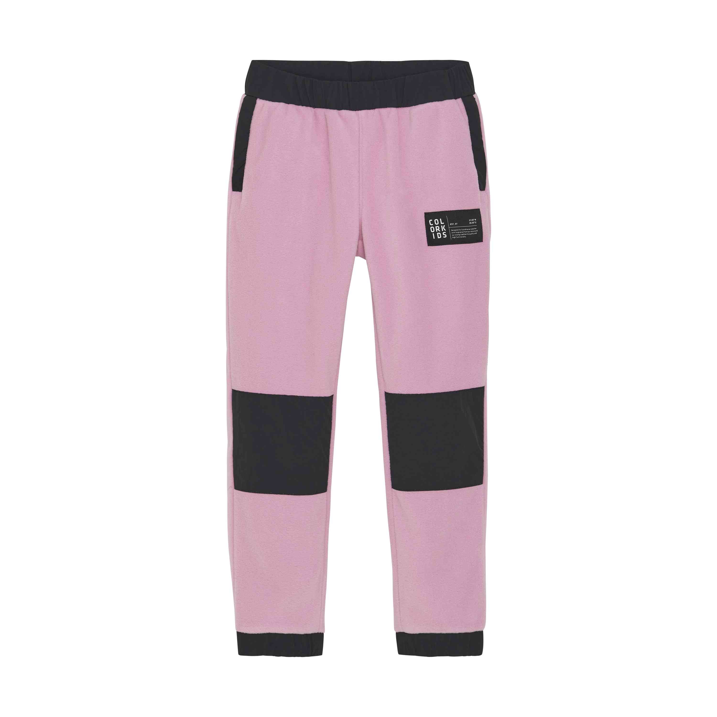 Ein Paar Color Kids - Fleece Hosen in Pink hat schwarze Knieflicken, schwarze Seitentaschen und einen elastischen Hosenbund aus dehnbarem Material. Ausserdem gibt es einen schwarzen rechteckigen Patch mit weissem Text auf dem linken Oberschenkel.