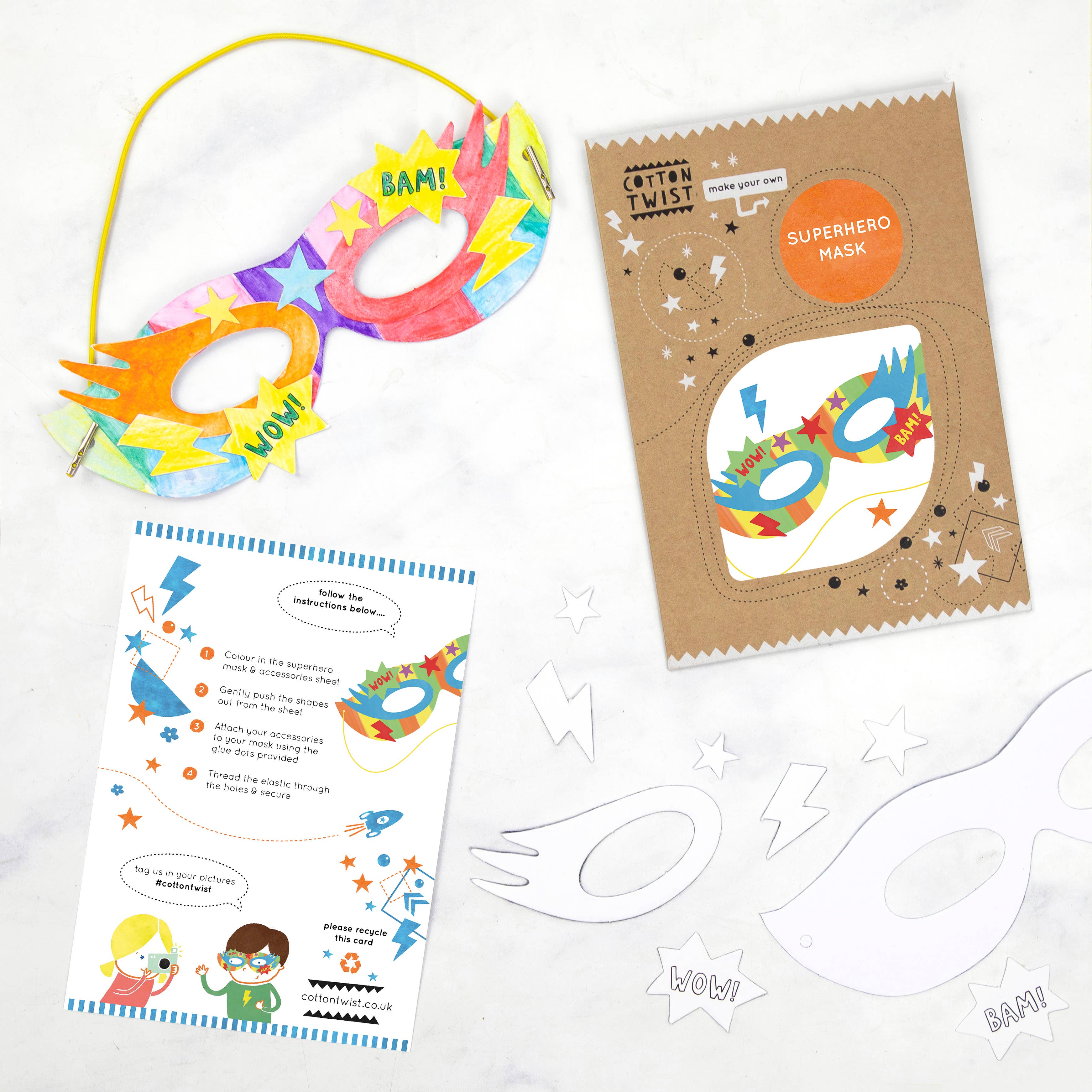 Farbenfrohes DIY-Maskenbastelset mit Superheldenmotiv von Cotton Twist, das ihre Cotton Twist - DIY Superhelden-Maske mit „BAM!“- und „WOW!“-Text präsentiert. Enthält eine Kartonverpackung aus umweltfreundlichen Materialien, eine gedruckte Anleitung und weiße Maskenvorlagen auf einer weißen Oberfläche. Perfekt für Kinder.