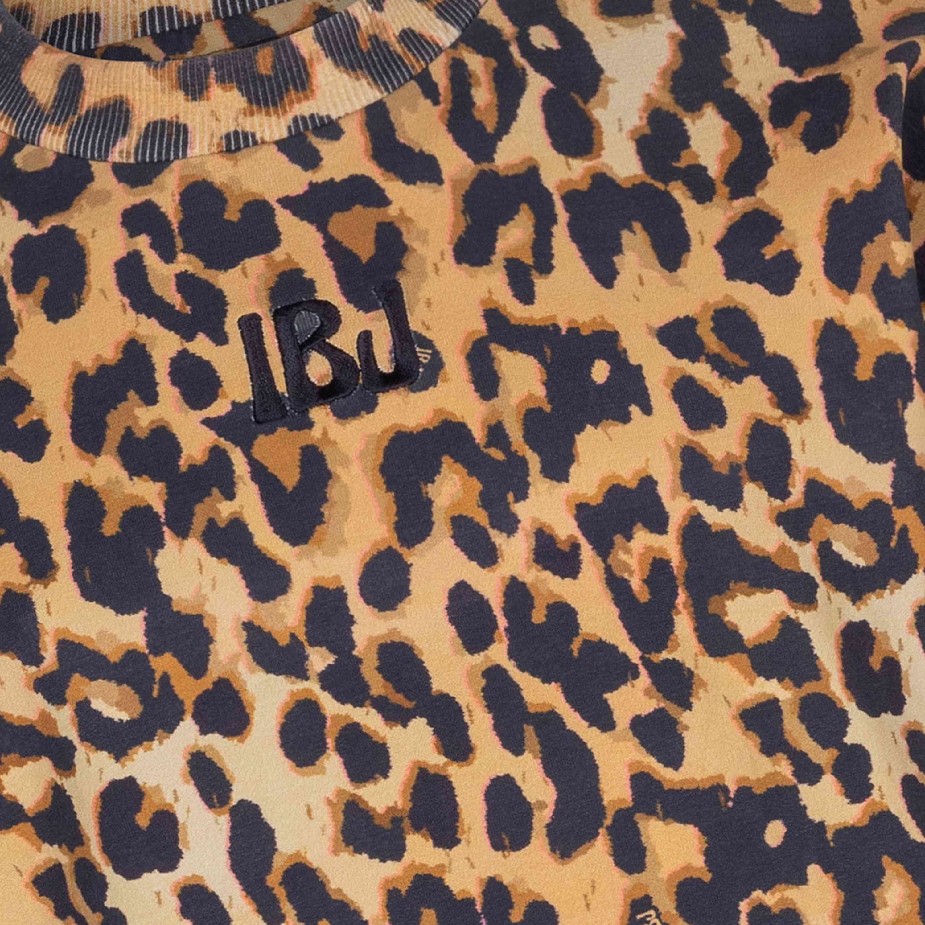 Nahaufnahme des Indian Blue Jeans - Pullover Leopard von Indian Blue Jeans, der einen Stoff mit einem kräftigen Leopardenmuster in Braun-, Gelb- und Schwarztönen zeigt. Auf dem Stoff sind die schwarzen gestickten Buchstaben „LBU“ zu sehen. Der Aufdruck weist große Farbflecken auf, die an einen klassischen Animalprint-Stil erinnern. Weitere Einzelheiten finden Sie in der Beschreibung.