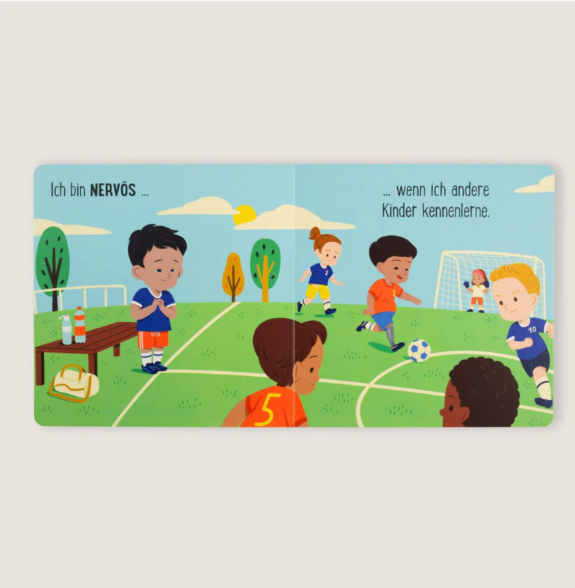 Eine illustrierte Kinderbuchseite zeigt Kinder, die auf einer Wiese Fußball spielen. Ein Kind sitzt nervös auf einer Bank. Der Text lautet auf Deutsch: „Ich bin nervös ... wenn ich andere Kinder kennenlerne.“ Gefühle sind für alle da! von nila kids.