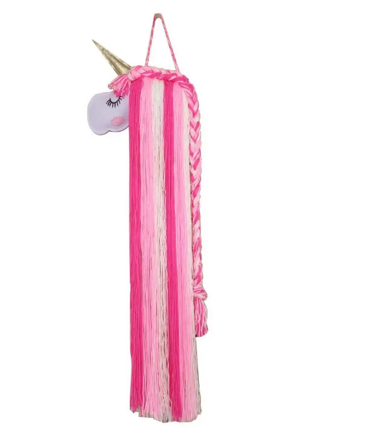 Ein handgefertigter Artilady - Einhorn-Haarspangenhalter für ein Kinderzimmer, mit langen rosa und weißen Garnsträngen, die die Mähne des Einhorns bilden, auf einer Seite geflochten. Das Einhorn hat ein weißes Gesicht mit einem goldenen Horn und einem geschlossenen Auge mit langen Wimpern. Es hängt an einer rosa Schlaufe, perfekt für die Einrichtung eines jungen Kinderzimmers.