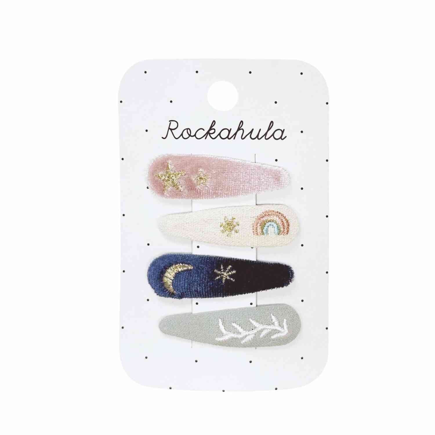 Ein Set mit vier Rockahula - Gesticktes Clipset mit Sternenhimmel-Motiven auf einer gepunkteten Trägerkarte, perfekt für frisurierte Babys. Die Clips sind in Pastellrosa mit Sternen, Zartrosa mit Regenbogen, Marineblau mit Mond und Sternen und Hellgrau mit weißen Blättern erhältlich. Jeder Clip ist mit kleinen, komplizierten Mustern bestickt.