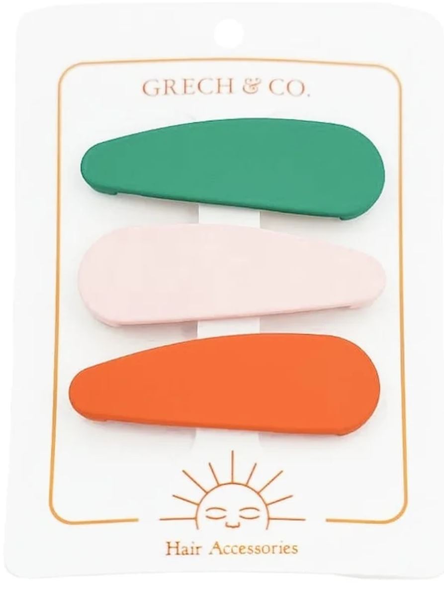 Eine Karte von „Grech und Co.“ zeigt drei ovale Haarspangen von Grech & Co. in den Farben Grün, Rosa und Orange. Unten auf der Karte befindet sich ein minimalistisches Sonnensymbol und der Text „Haarschmuck“. Diese Spangen sind perfekt für Kinder und sind stilvoll gestaltet, um nachhaltige Modeentscheidungen zu ergänzen.