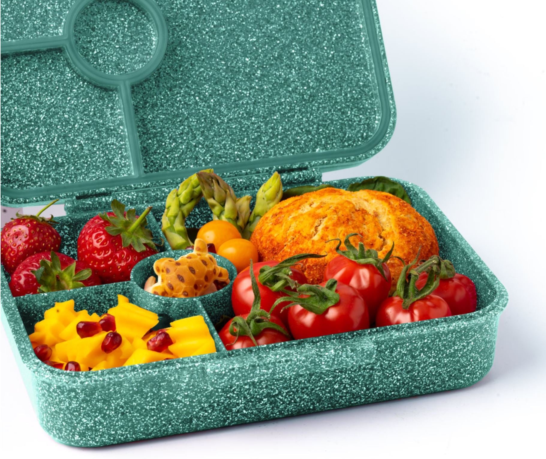 Eine grüne Lekkabox – Lunchbox Glamour mit verschiedenen Lebensmitteln, darunter Kirschtomaten, eine mit Granatapfelkernen verzierte Käsescheibe, Erdbeeren, Brombeeren, ein Stück Brot, Spargeln, gelbe Paprikascheiben, Kirschtomaten und ein Stück Honigwabe – perfekt als Znünibox für den Kindergarten.