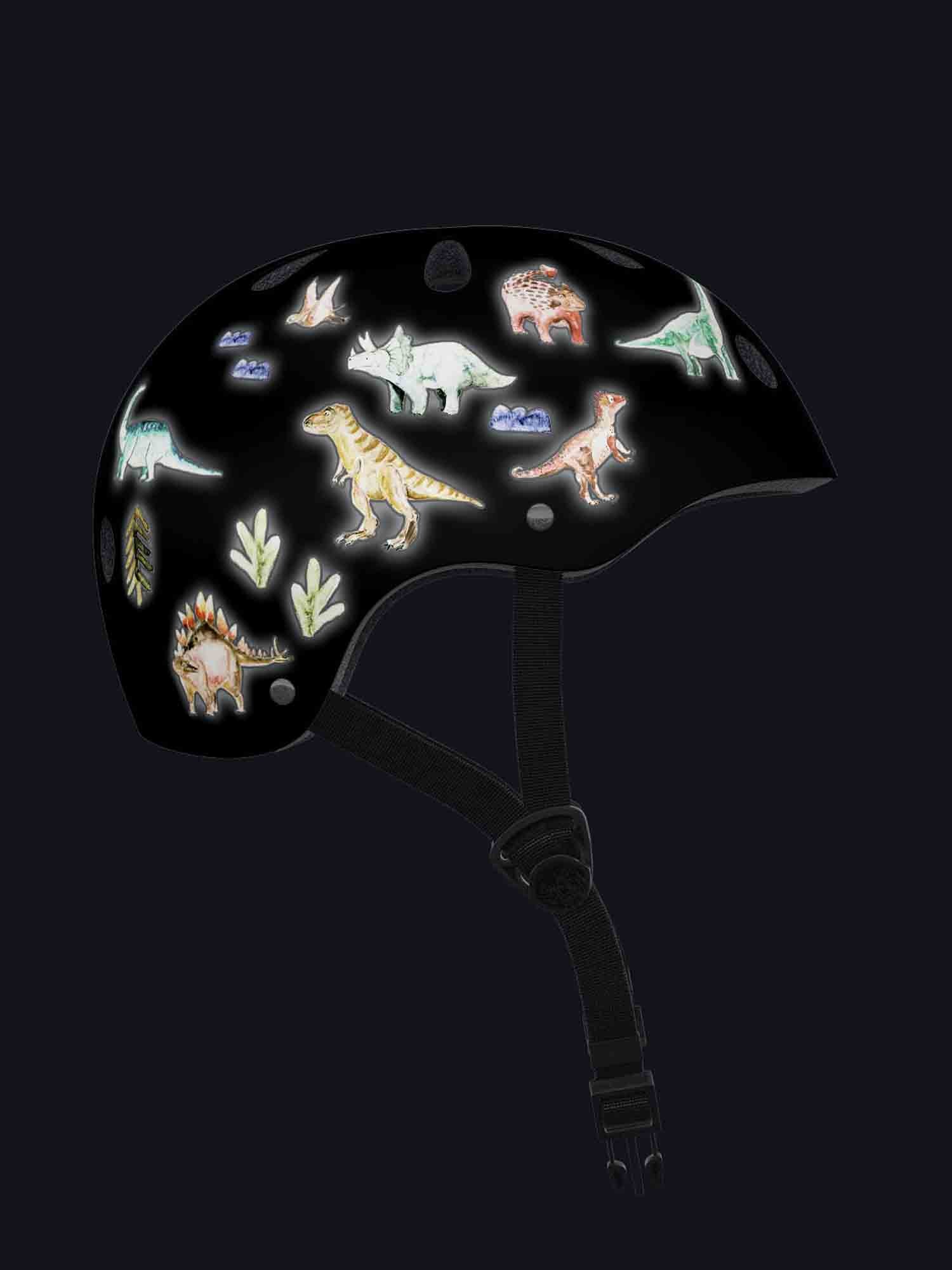 Ein schwarzer Helm für ein Baby ist mit bunten, leuchtenden Dinosaurieraufklebern von Halfbird verziert – Set Reflektierende Aufkleber: Dino von Halfbird, darunter ein T-Rex, ein Triceratops, ein Stegosaurus und verschiedene andere Dinosaurierillustrationen. Der Helm hat einen schwarzen verstellbaren Kinnriemen und ist auf einem dunklen Hintergrund angebracht.